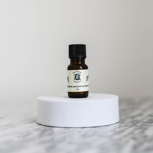 10ml amber bottle of Eucalyptus Essential Oil by Quen T’essentielle, displayed on a minimalist white pedestal with clean marble background – natural remedy for respiratory support and mental clarity.