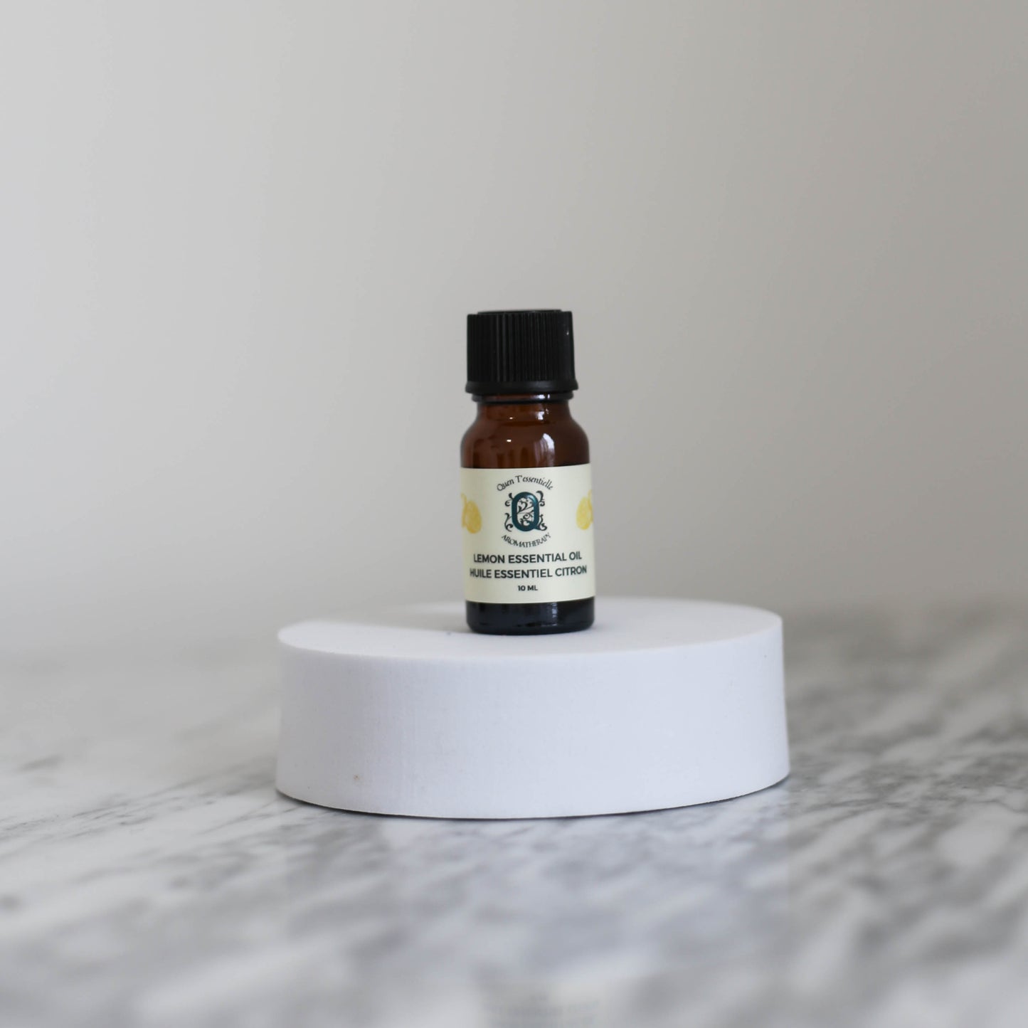 Small bottle of lemon essential oil on a white pedestal with a light gray background