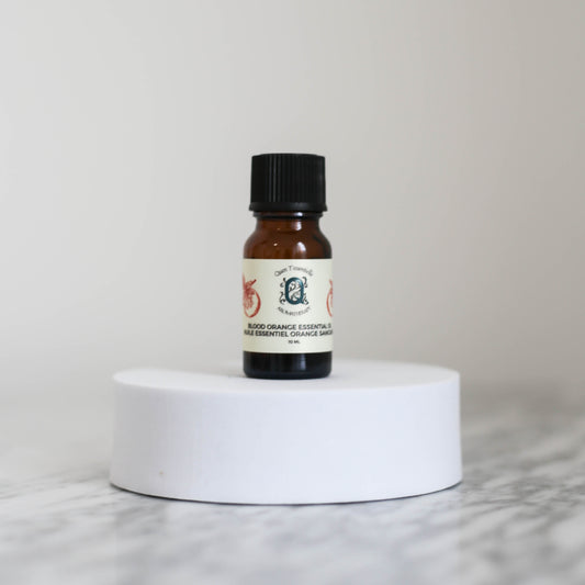 Blood Orange Essential oil 10ml bottle by Quen T’essentielle Aromatherapy, displayed on a white pedestal with minimalist background – natural essential oil for uplifting and refreshing aromatherapy use.