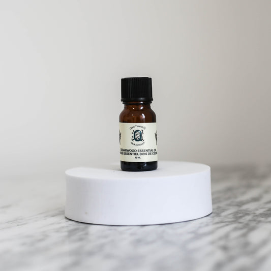 Cedarwood Essential Oil 10ml bottle by Quen T’essentielle Aromatherapy, displayed on a white pedestal with a neutral background – natural essential oil for grounding, skin support, and aromatherapy.