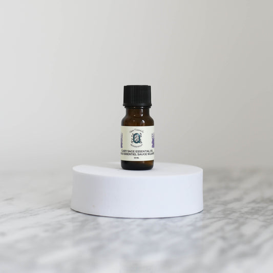 10ml amber glass bottle of Clary Sage Essential Oil by Quen T’essentielle, displayed on a white pedestal with minimalist background – natural aromatherapy product for mood support and well-being.