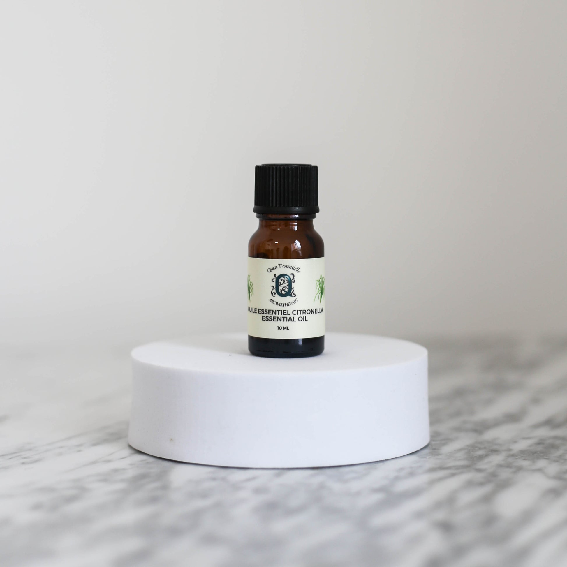 Citronella Essential Oil 10ml bottle by Quen T’essentielle Aromatherapy, displayed on a white pedestal with a minimalist background – natural insect repellent and mood-boosting essential oil.