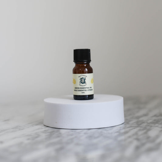 Small bottle of lemon essential oil on a white pedestal with a light gray background