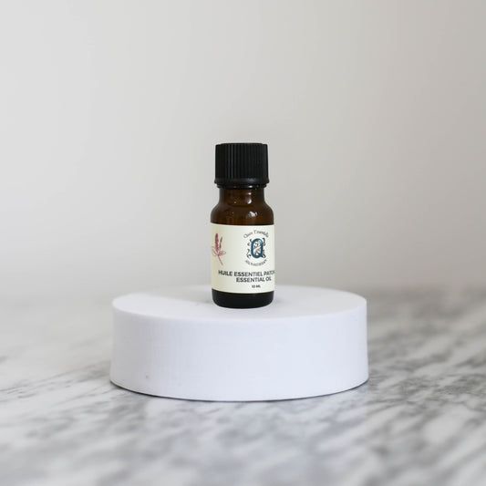 Small amber glass bottle of Patchouli essential oil with a label on a white marble surface.
